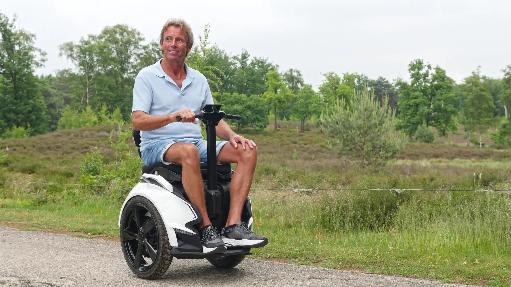 Lachende man op een witte elektrische balansrolstoel over een verhard pad in een groen natuurgebied