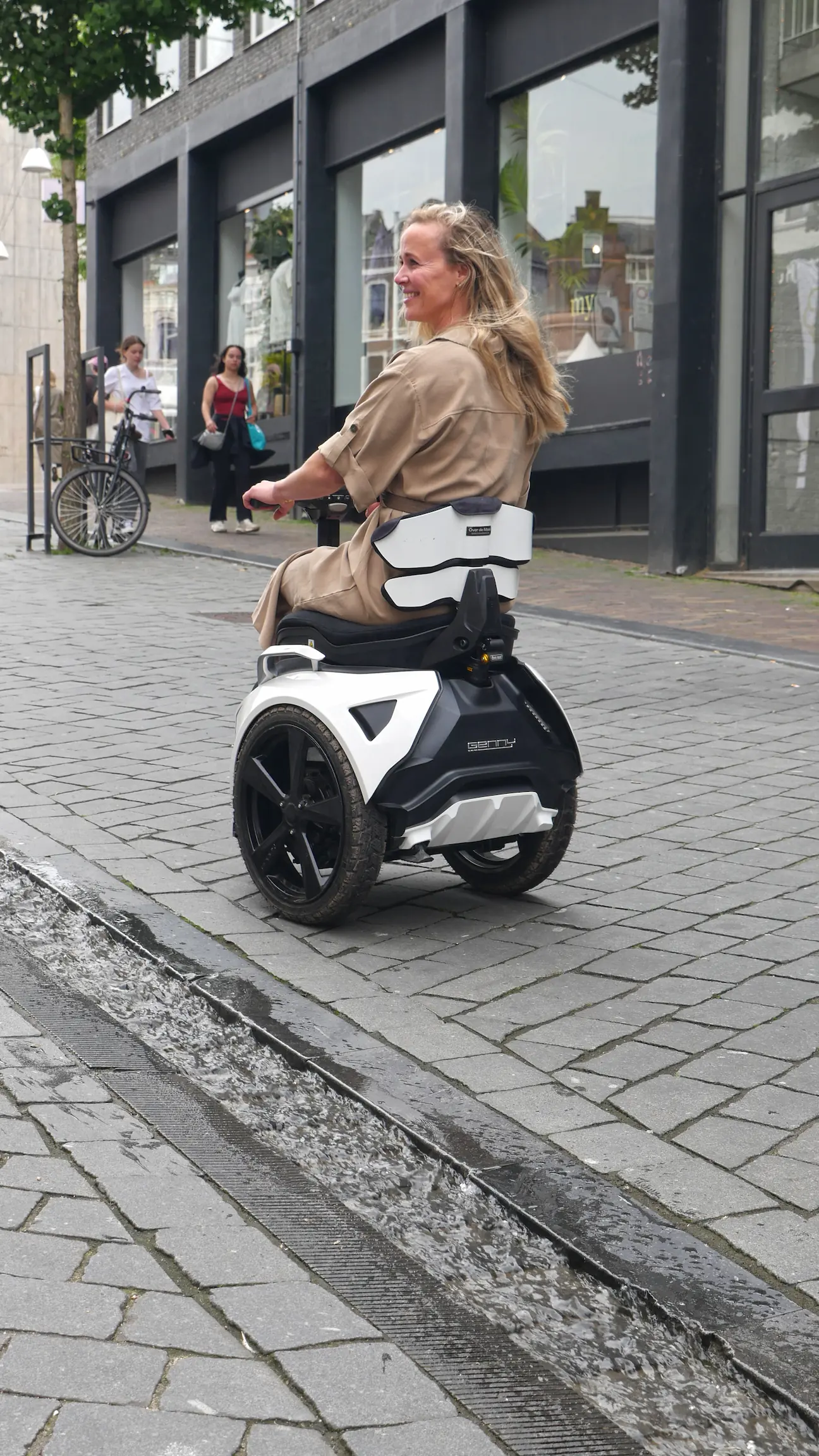 Blonde vrouw op een witte balansrolstoel rijdt lachend over natte stadsklinkers