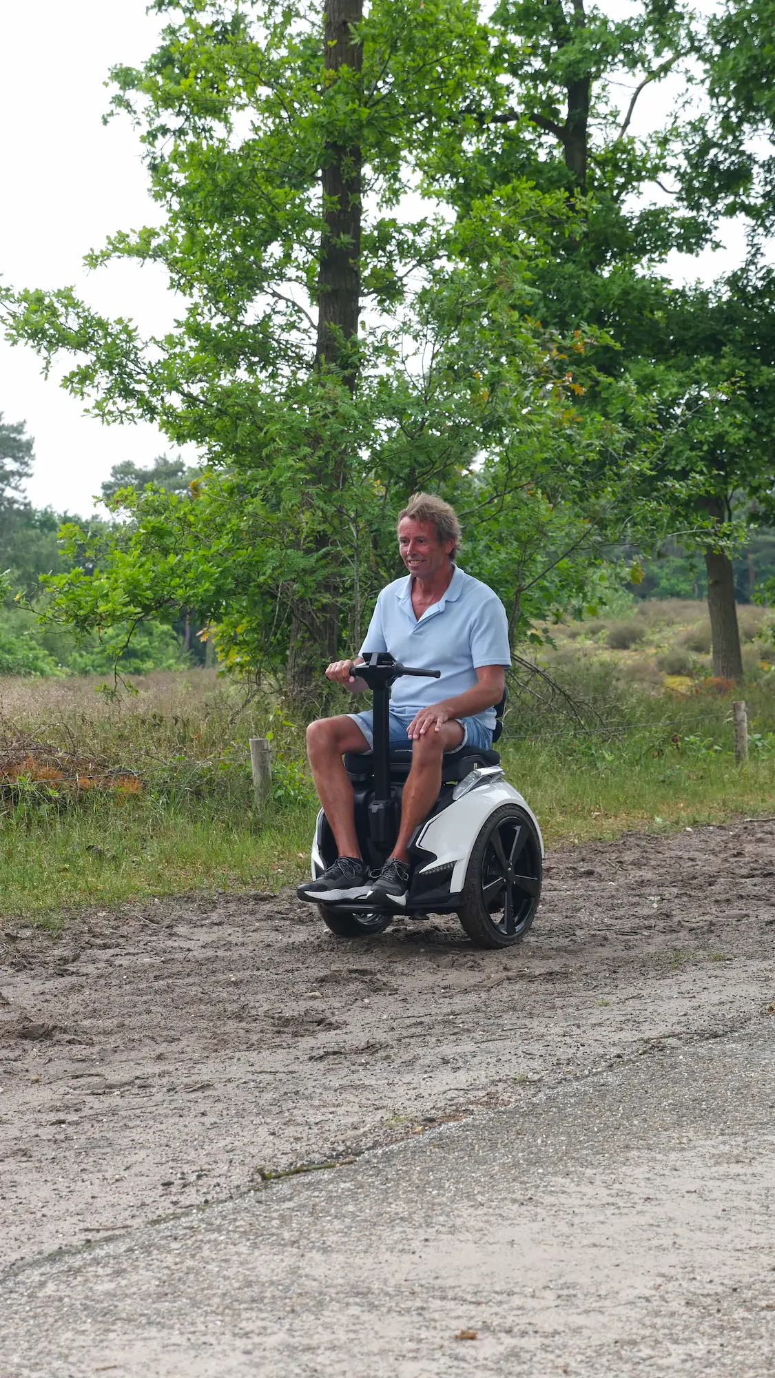 Man op een witte balansrolstoel rijdt over een ongelijk grindpad langs de bosrand