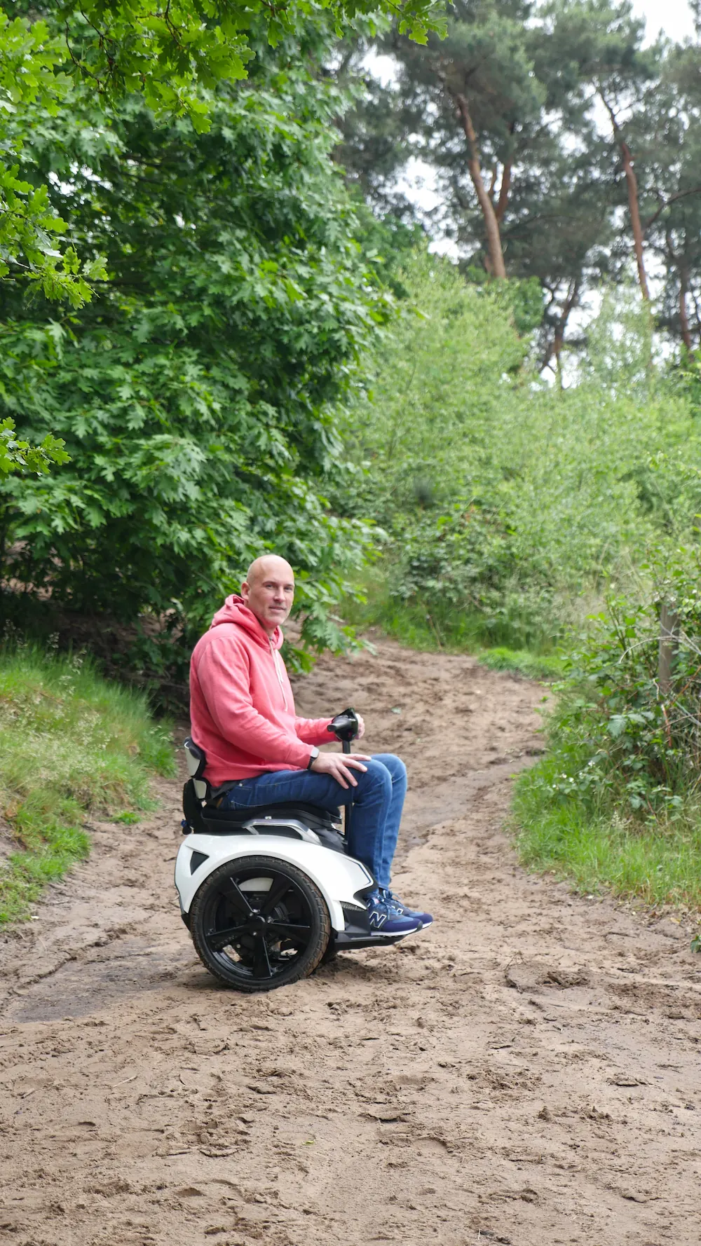 Man op een witte balansrolstoel op een smal zandpad in een dichtbegroeid bos